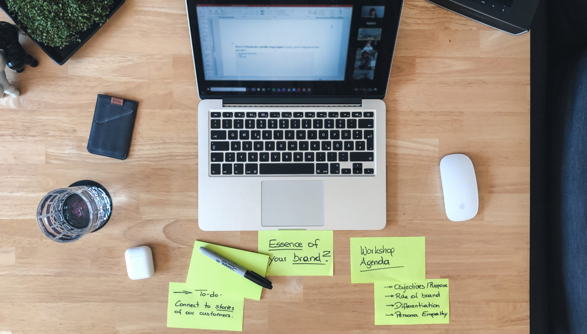 Desktop with Apple laptop, Airpods and magic mouse with some post it notes about a workshop agenda
